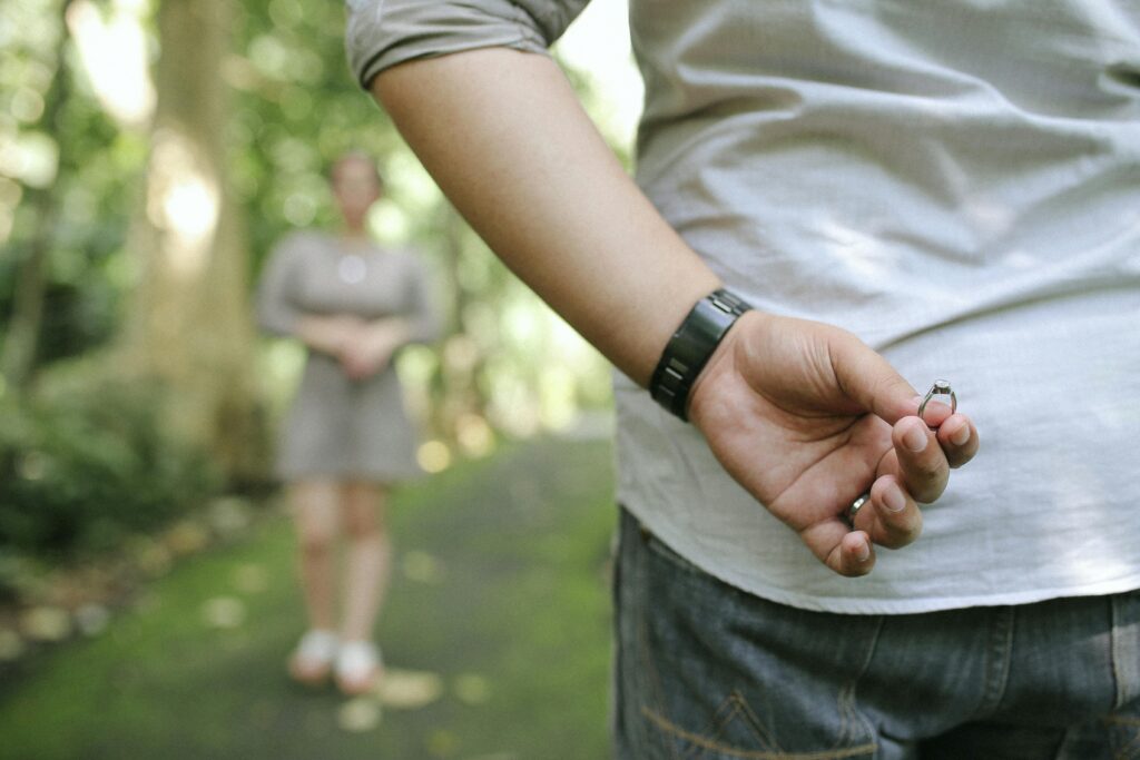 pexels photo 1480284 1480284 A man hides an engagement ring behind his back, preparing to propose in a picturesque park setting.