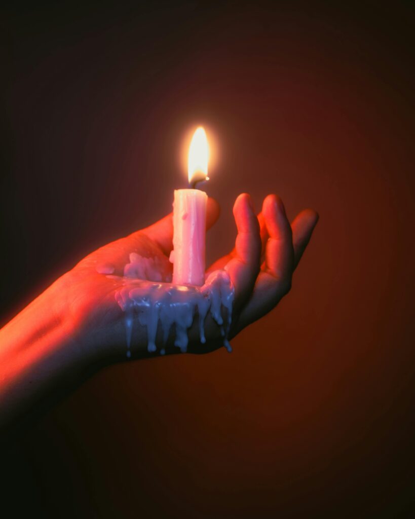 pexels photo 17400155 17400155 A close-up of a hand holding a burning candle with melting wax, against a red background.