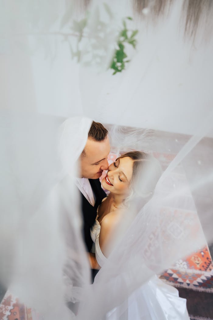 Aerial view of a joyful couple embracing beneath a wedding veil, conveying romance and bliss.