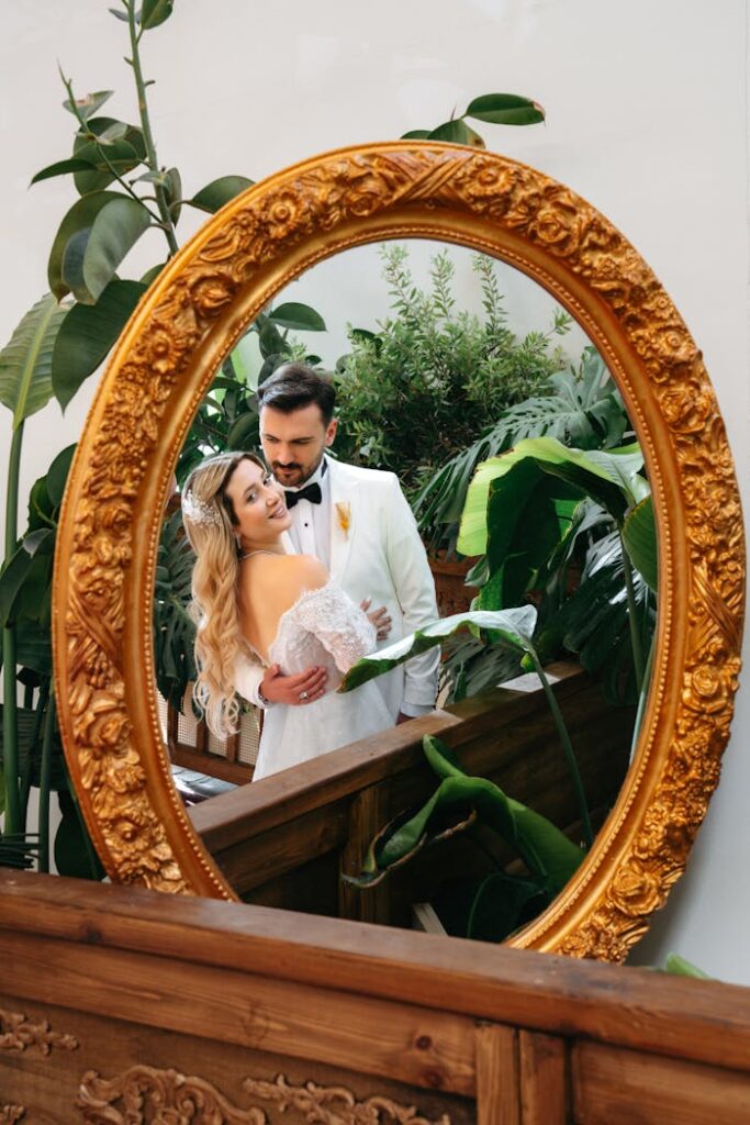 pexels photo 33979990 Charming wedding couple embraces reflected in an ornate antique mirror surrounded by lush greenery.