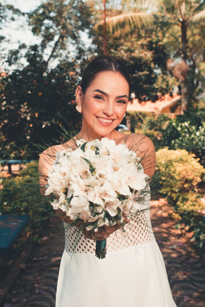Bride holding a white flower bouquet outdoors, showcasing a joyful and serene wedding moment.