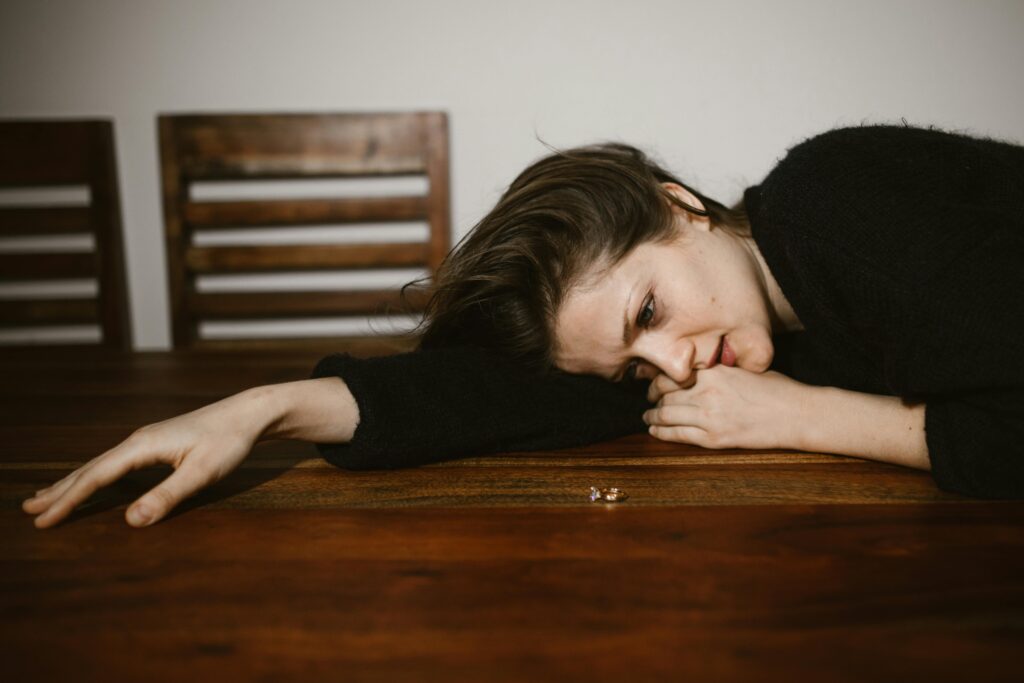 pexels photo 6670261 6670261 A woman lying on a wooden table, reflecting on a wedding ring, portraying emotions of sadness and contemplation.